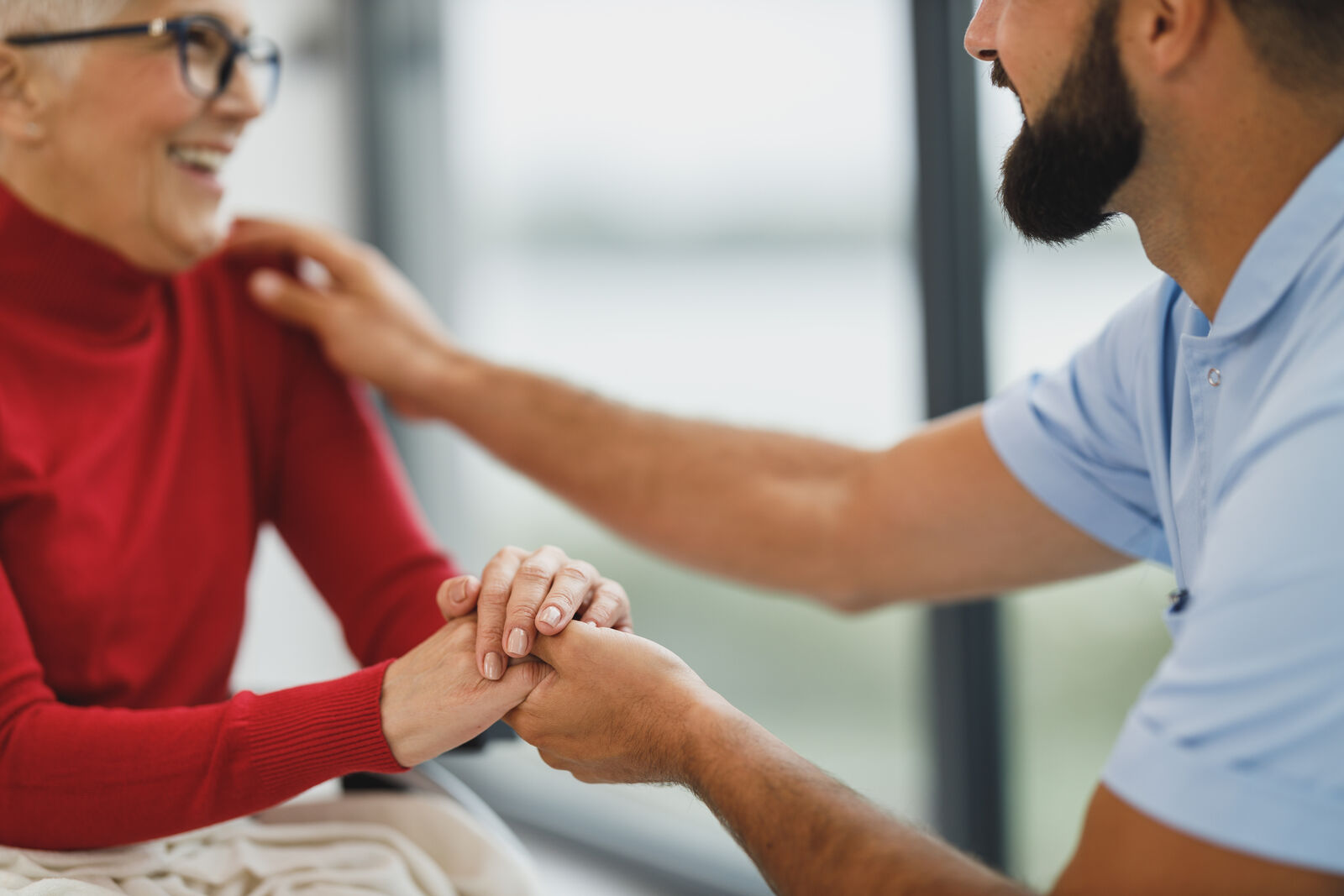 Une main posée sur celle d'une personne âgée souriante, en signe d'accompagnement